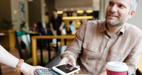 Homme dans un café pose son téléphone sur un terminal de paiement