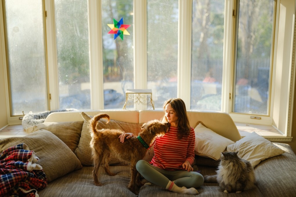 Photo d’une femme assise sur son canapé avec son chien et son chat pour un article sur l’achat de maison seul.