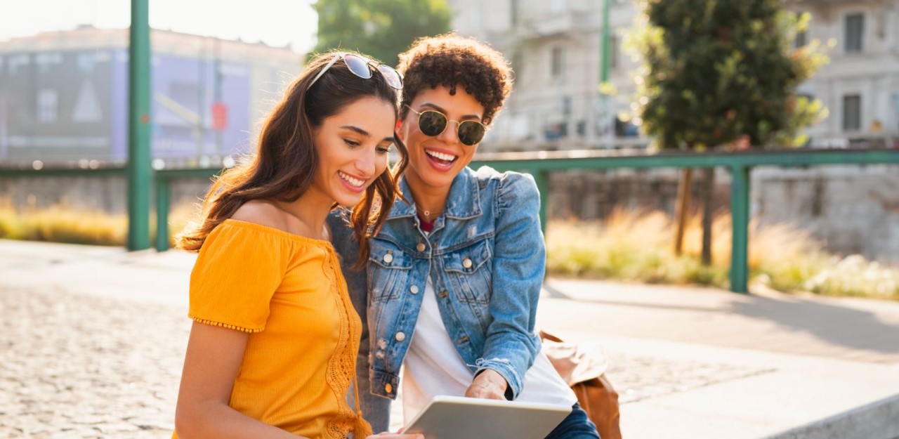 Photo de deux femmes dehors consultant une tablette en souriant