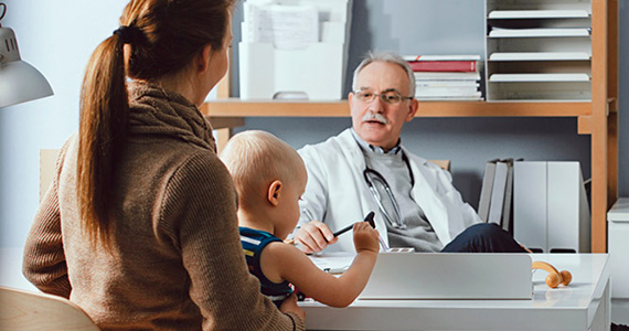 Photo d’un médecin dans son cabinet discutant avec une patiente tenant un bébé sur ses genoux 
